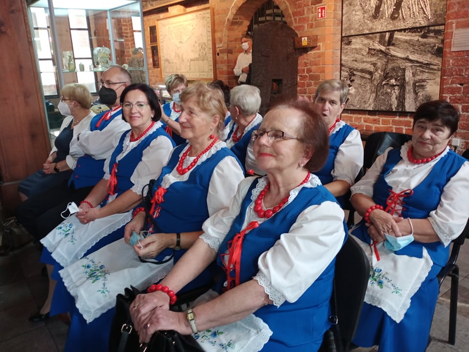 Grupa seniorów ubrana w lokalne stroje ustawiona do zdjęcia grupowego. W środku dwie kobiety ubrane na czarno. 