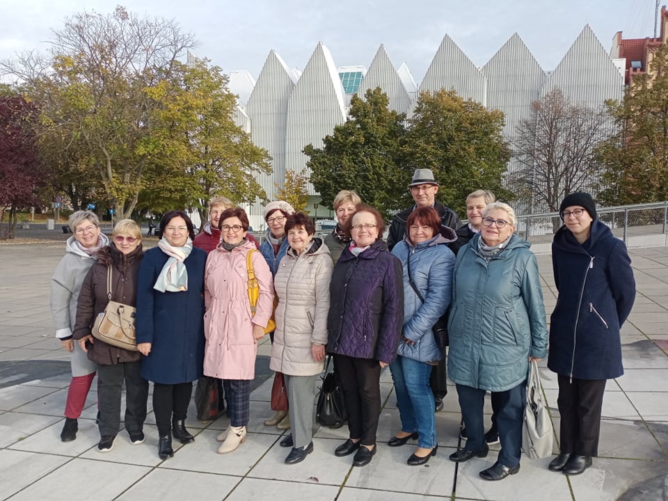 Grupa seniorów ubrana w lokalne stroje ustawiona do zdjęcia grupowego. W środku dwie kobiety ubrane na czarno. 