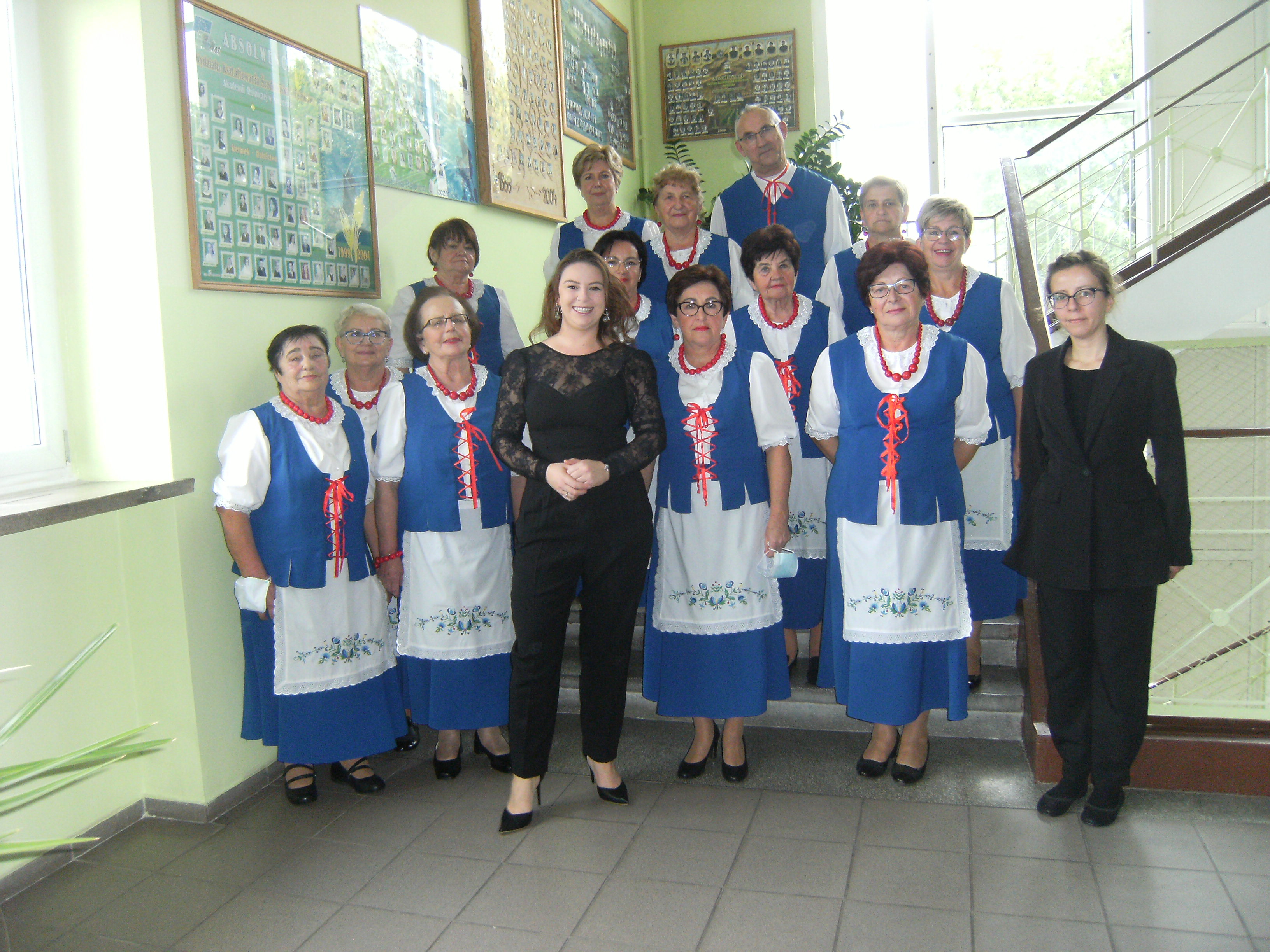Grupa seniorów ubrana w lokalne stroje ustawiona do zdjęcia grupowego. W środku dwie kobiety ubrane na czarno. 